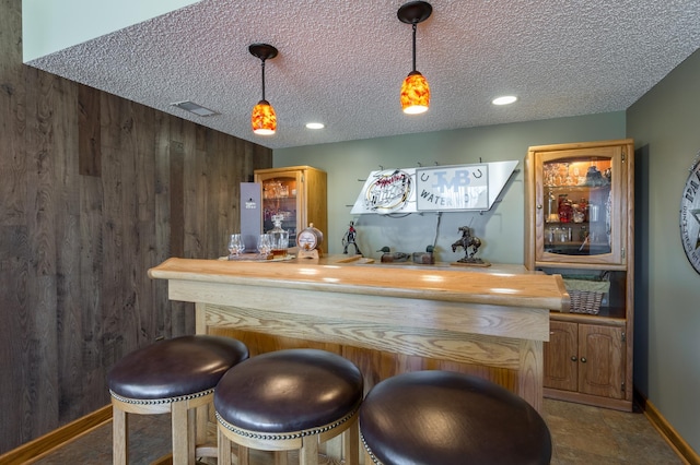 bar featuring butcher block counters, wooden walls, and a textured ceiling