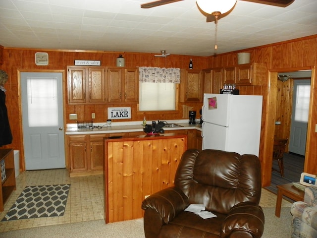 kitchen featuring white refrigerator, sink, and wood walls