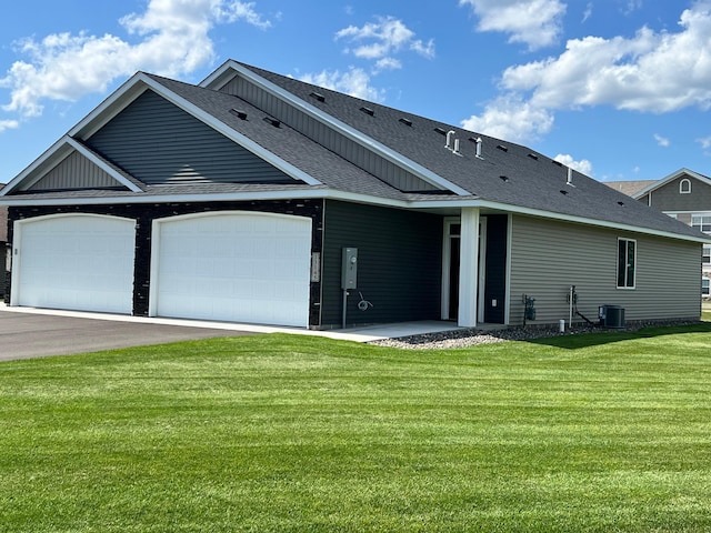 rear view of property with central AC unit, a garage, and a lawn