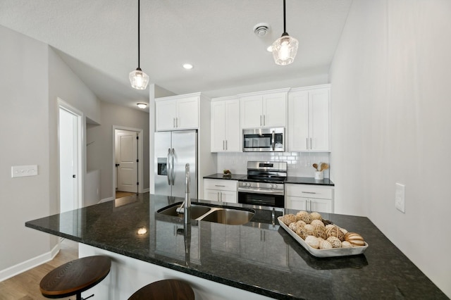 kitchen with sink, appliances with stainless steel finishes, hanging light fixtures, white cabinets, and dark stone counters