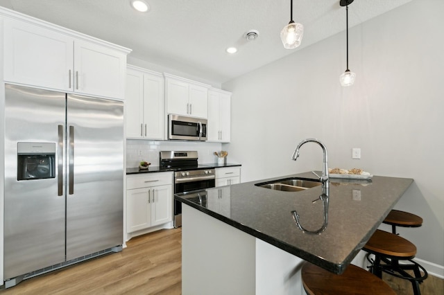 kitchen with a sink, visible vents, appliances with stainless steel finishes, backsplash, and light wood finished floors