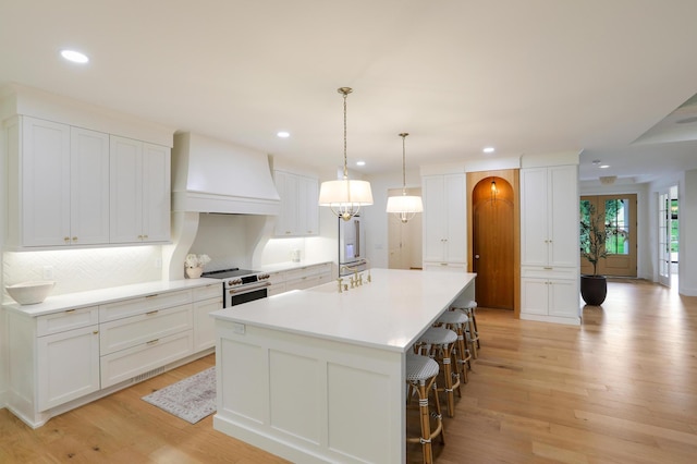 kitchen featuring white cabinetry, hanging light fixtures, electric range oven, custom range hood, and a large island