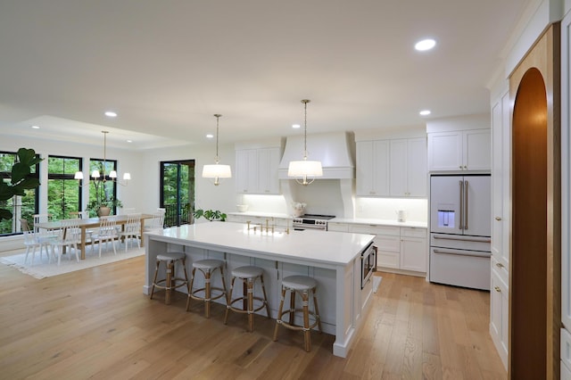 kitchen featuring appliances with stainless steel finishes, a breakfast bar, white cabinets, a large island with sink, and light hardwood / wood-style floors