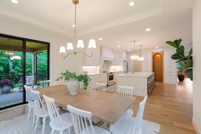 dining area featuring a raised ceiling, light wood-type flooring, and a notable chandelier