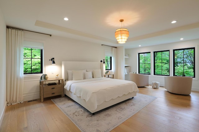 bedroom featuring multiple windows, a tray ceiling, and light hardwood / wood-style flooring