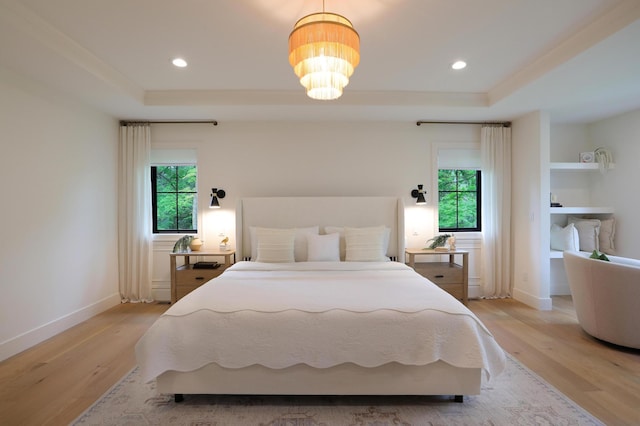 bedroom with light hardwood / wood-style floors, a raised ceiling, and a chandelier