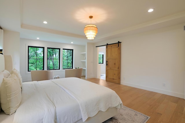 bedroom with a raised ceiling, a barn door, and light hardwood / wood-style floors