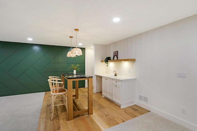 bar featuring sink, white cabinetry, hanging light fixtures, wooden walls, and light wood-type flooring