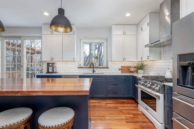 kitchen featuring appliances with stainless steel finishes, blue cabinets, sink, white cabinets, and wall chimney range hood