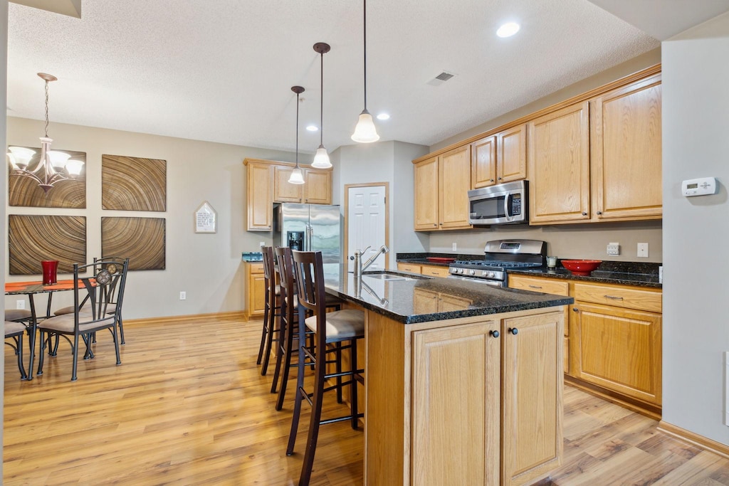 kitchen featuring appliances with stainless steel finishes, pendant lighting, an island with sink, sink, and light hardwood / wood-style floors