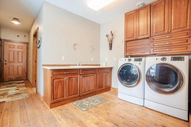 clothes washing area with independent washer and dryer, sink, light hardwood / wood-style flooring, and cabinets