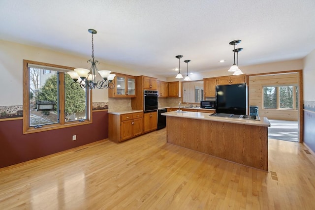 kitchen featuring pendant lighting, light wood-type flooring, a kitchen island, and black appliances