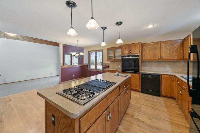 kitchen with decorative light fixtures, a center island with sink, backsplash, and black appliances