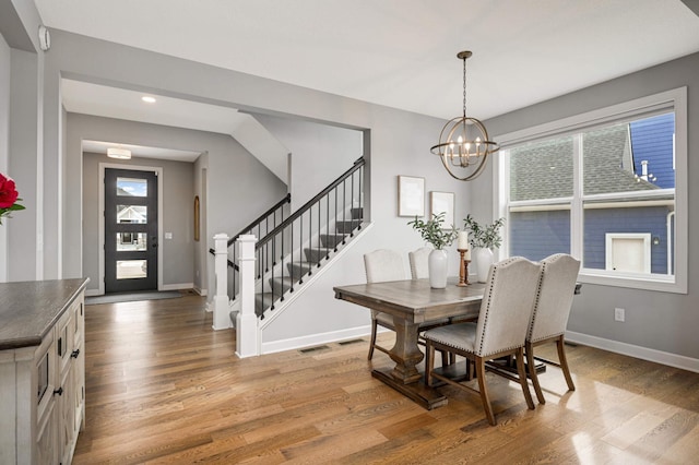 dining room with light wood-type flooring, stairs, baseboards, and a notable chandelier