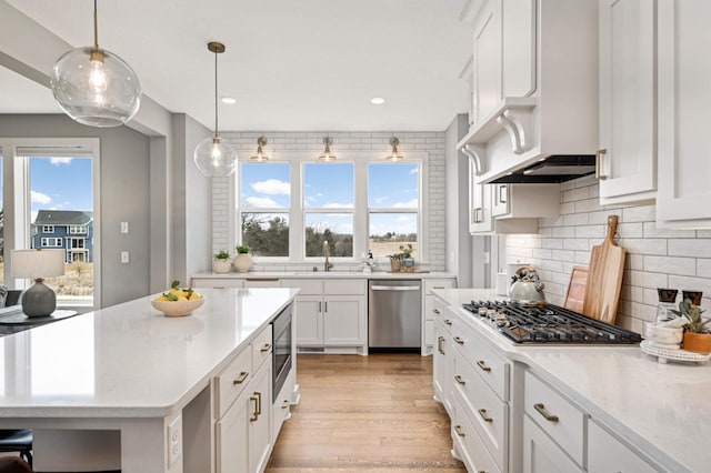 kitchen featuring decorative light fixtures, stainless steel appliances, light wood-type flooring, white cabinetry, and a sink