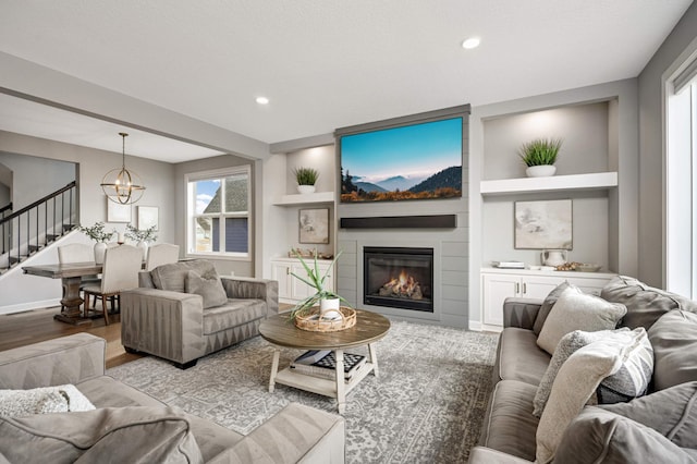 living room featuring light wood-style flooring, recessed lighting, a large fireplace, a notable chandelier, and stairs