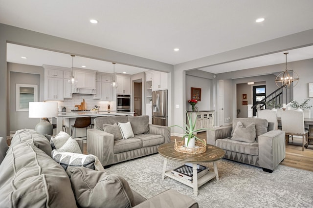 living room with recessed lighting, light wood-style flooring, a chandelier, baseboards, and stairs