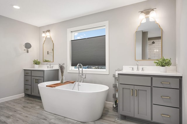 bathroom featuring two vanities, a soaking tub, a sink, and baseboards