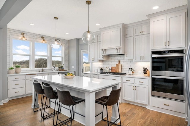 kitchen featuring light wood finished floors, a kitchen breakfast bar, light countertops, stainless steel appliances, and backsplash