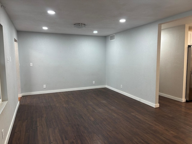 finished below grade area featuring freestanding refrigerator, dark wood-style flooring, visible vents, and baseboards