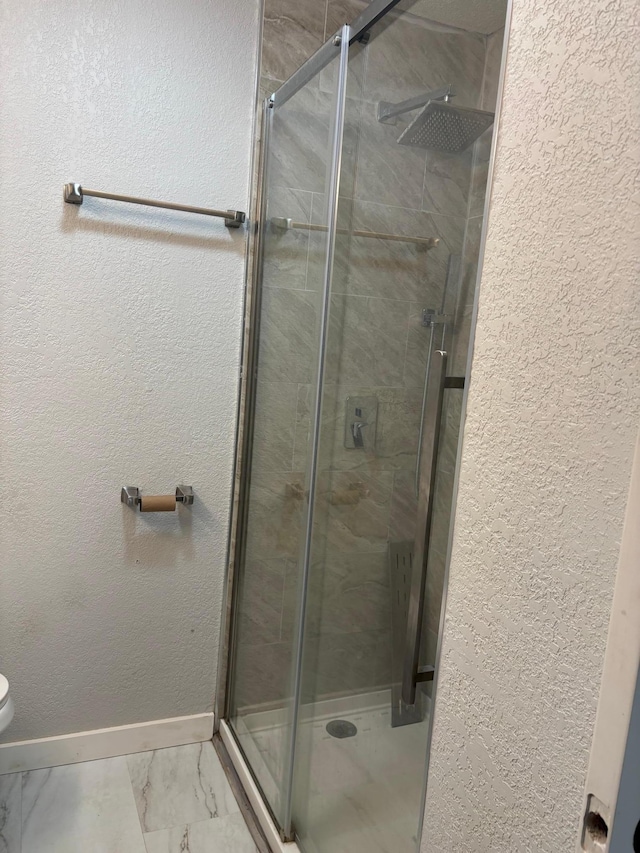 bathroom with marble finish floor, a shower stall, baseboards, and a textured wall