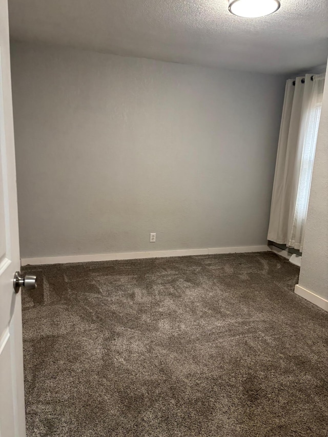 unfurnished room featuring a textured ceiling, dark carpet, and baseboards