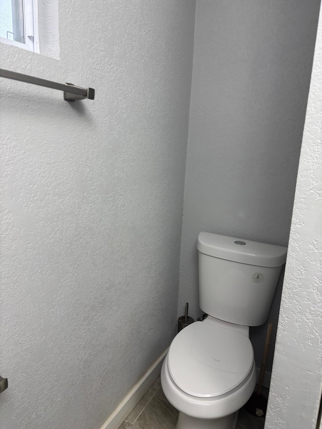 bathroom featuring baseboards, a textured wall, and toilet