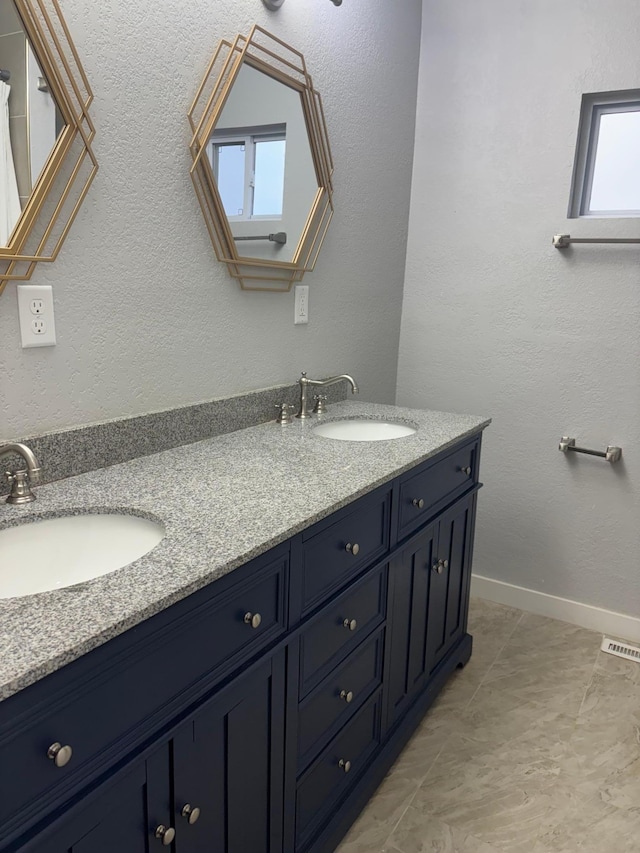 full bathroom with a textured wall, a sink, baseboards, and double vanity