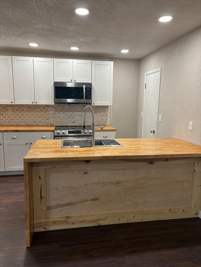 kitchen with stainless steel microwave, decorative backsplash, dark wood-type flooring, a sink, and wood counters