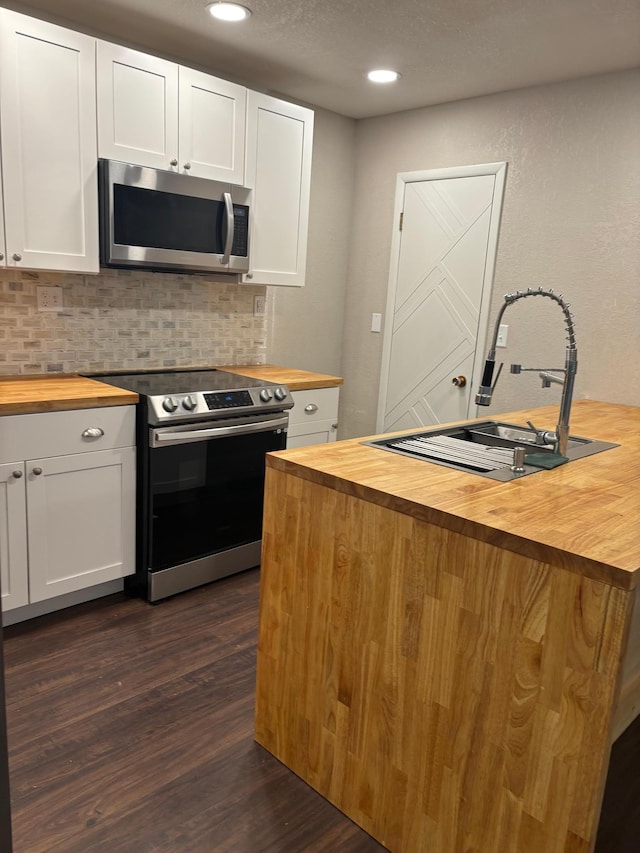 kitchen featuring butcher block countertops, appliances with stainless steel finishes, dark wood-type flooring, a sink, and backsplash