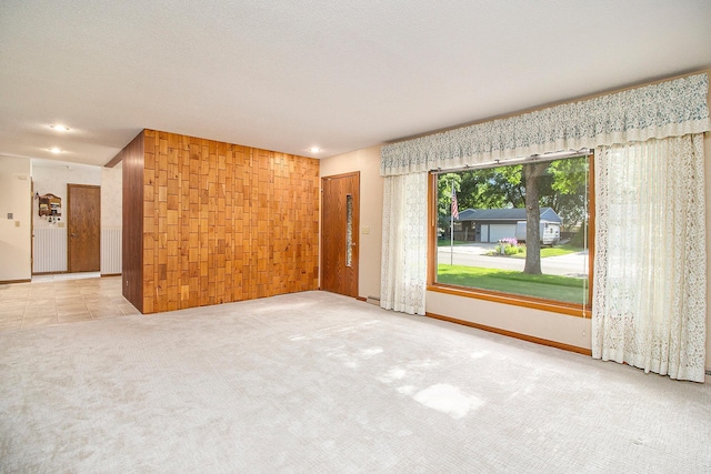 empty room featuring light carpet, a textured ceiling, and wood walls