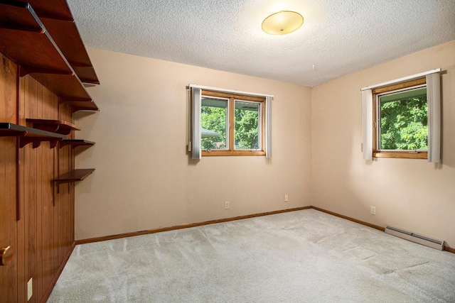 carpeted spare room with plenty of natural light, a baseboard heating unit, and a textured ceiling