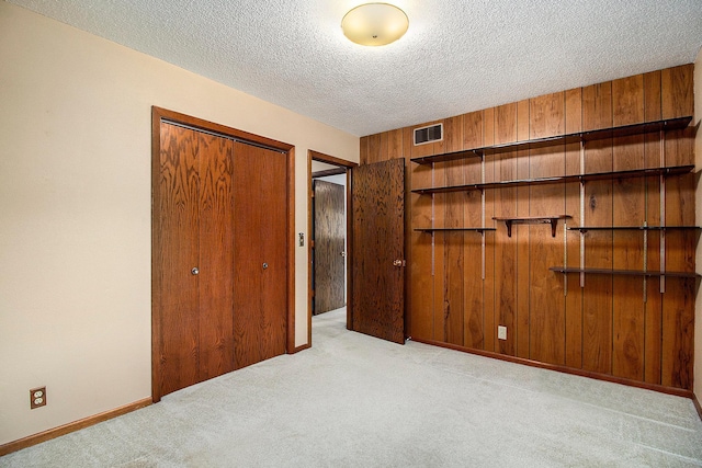 unfurnished bedroom featuring wooden walls, light colored carpet, a textured ceiling, and a closet