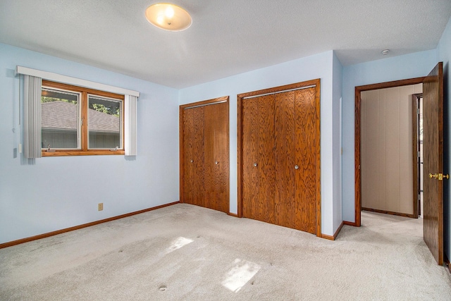 unfurnished bedroom featuring multiple closets, light colored carpet, and a textured ceiling