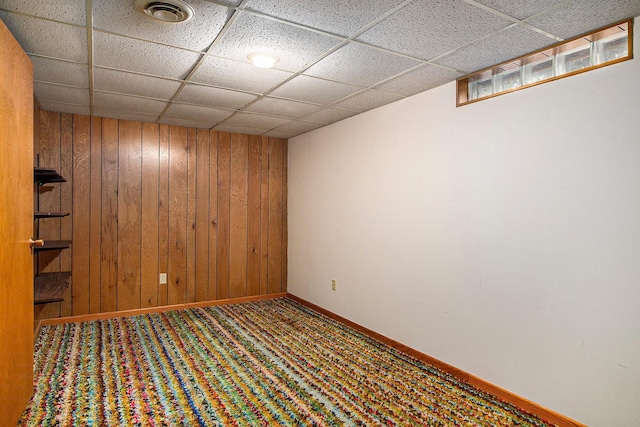 carpeted empty room with a drop ceiling and wood walls