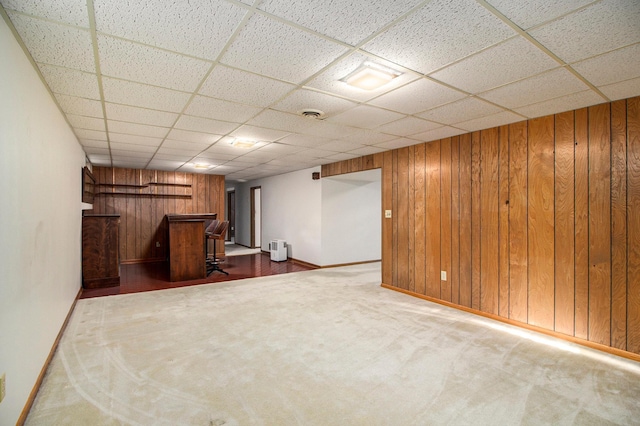 basement featuring carpet floors, a drop ceiling, and wooden walls