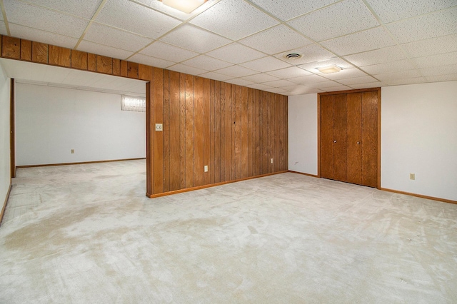 basement featuring light carpet, a paneled ceiling, and wood walls