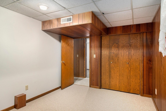 unfurnished bedroom featuring a paneled ceiling, light colored carpet, wooden walls, and a closet