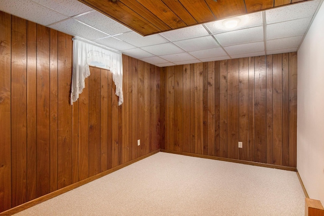 basement with a paneled ceiling, carpet flooring, and wood walls