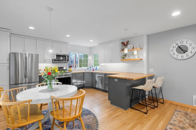 kitchen with butcher block countertops, appliances with stainless steel finishes, white cabinets, decorative light fixtures, and light wood-type flooring