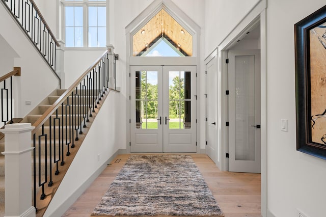 entrance foyer with french doors, a towering ceiling, and light wood-type flooring