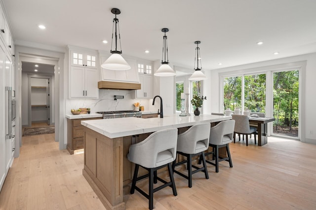 kitchen featuring decorative light fixtures, white cabinetry, light stone countertops, light wood-type flooring, and a spacious island