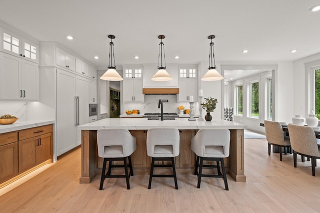 kitchen featuring a kitchen island with sink, white cabinetry, pendant lighting, and a breakfast bar area