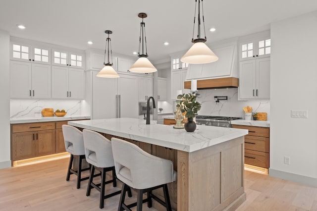 kitchen featuring a spacious island, premium range hood, white cabinetry, light stone counters, and decorative light fixtures