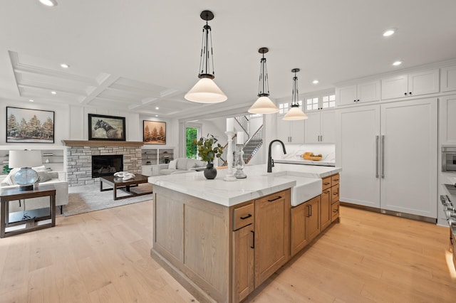 kitchen featuring sink, white cabinetry, light stone counters, pendant lighting, and a kitchen island with sink