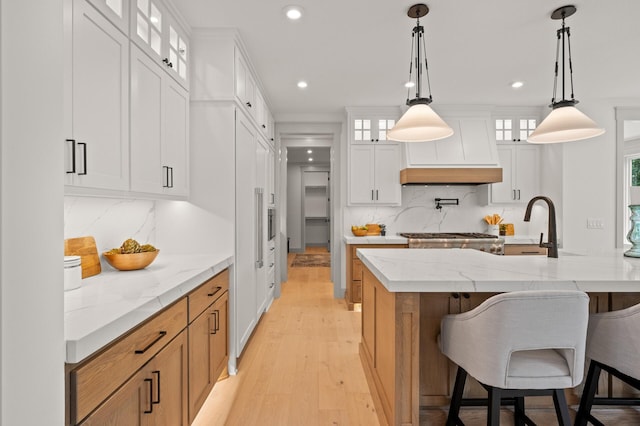 kitchen featuring a large island with sink, light stone countertops, hanging light fixtures, and white cabinets