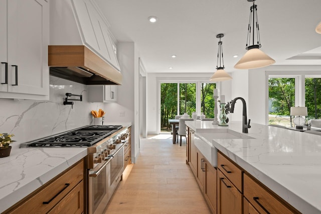 kitchen featuring pendant lighting, white cabinetry, sink, range with two ovens, and light stone counters