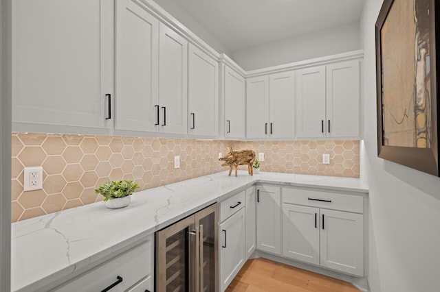 kitchen featuring wine cooler, white cabinetry, light stone countertops, and tasteful backsplash