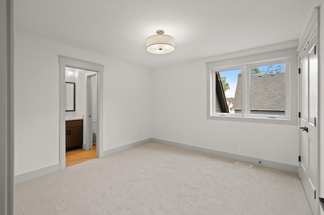 unfurnished bedroom featuring connected bathroom and light colored carpet