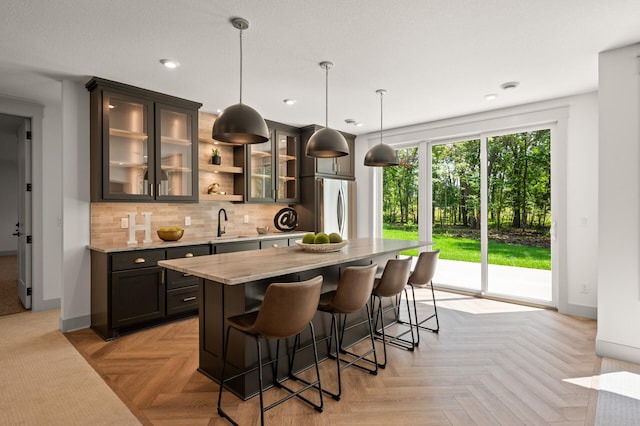 kitchen featuring light stone counters, decorative light fixtures, a center island, stainless steel fridge, and light parquet floors